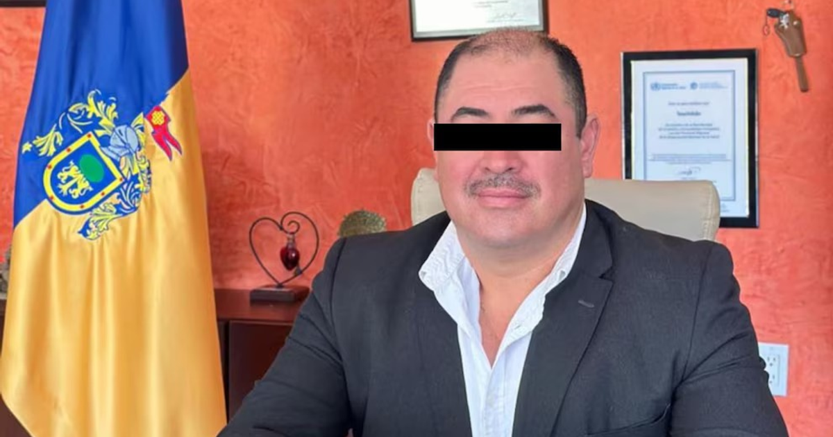 Hombre en oficina con bandera y documentos enmarcados, relacionado con audiencia de imputación en Jalisco.