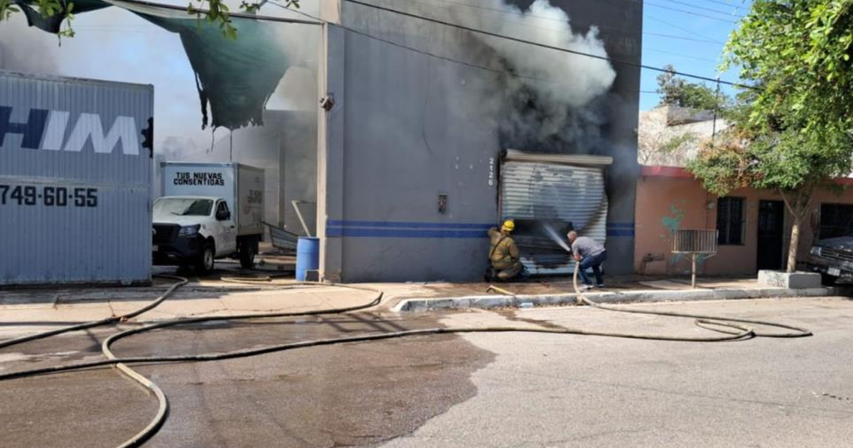 Incendio en taller de Culiacán tras balacera, bombero con manguera y humo denso