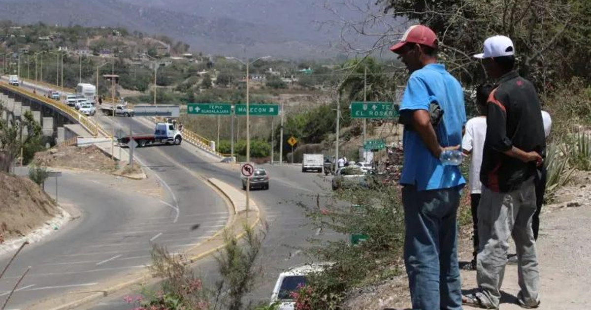 Hombres observando el tráfico en una carretera con un puente al fondo, relacionado con el bloqueo en el puente de Rosario.
