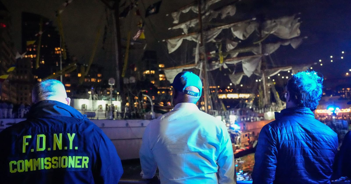 Tres personas de espaldas observando un barco en el puerto de Nueva York por la noche.
