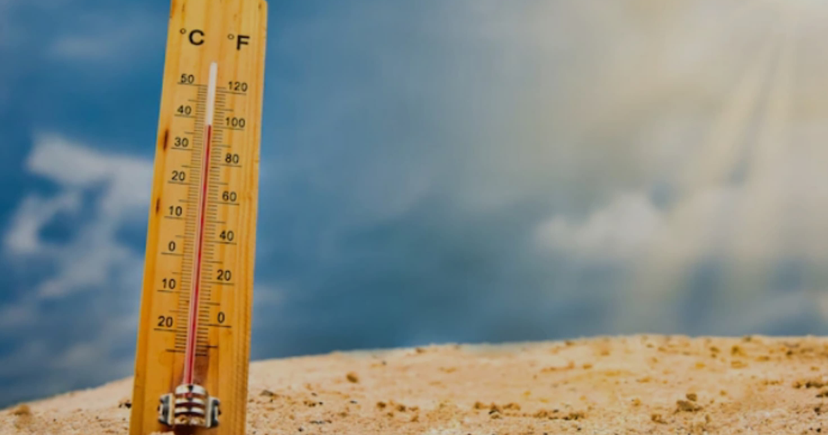 Termómetro de madera en arena con cielo nublado y luz solar
