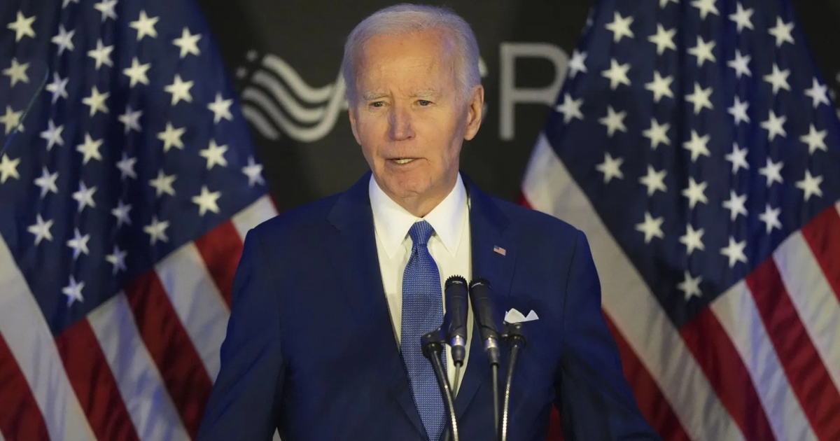 Hombre hablando en un evento político con banderas de EE.UU. de fondo