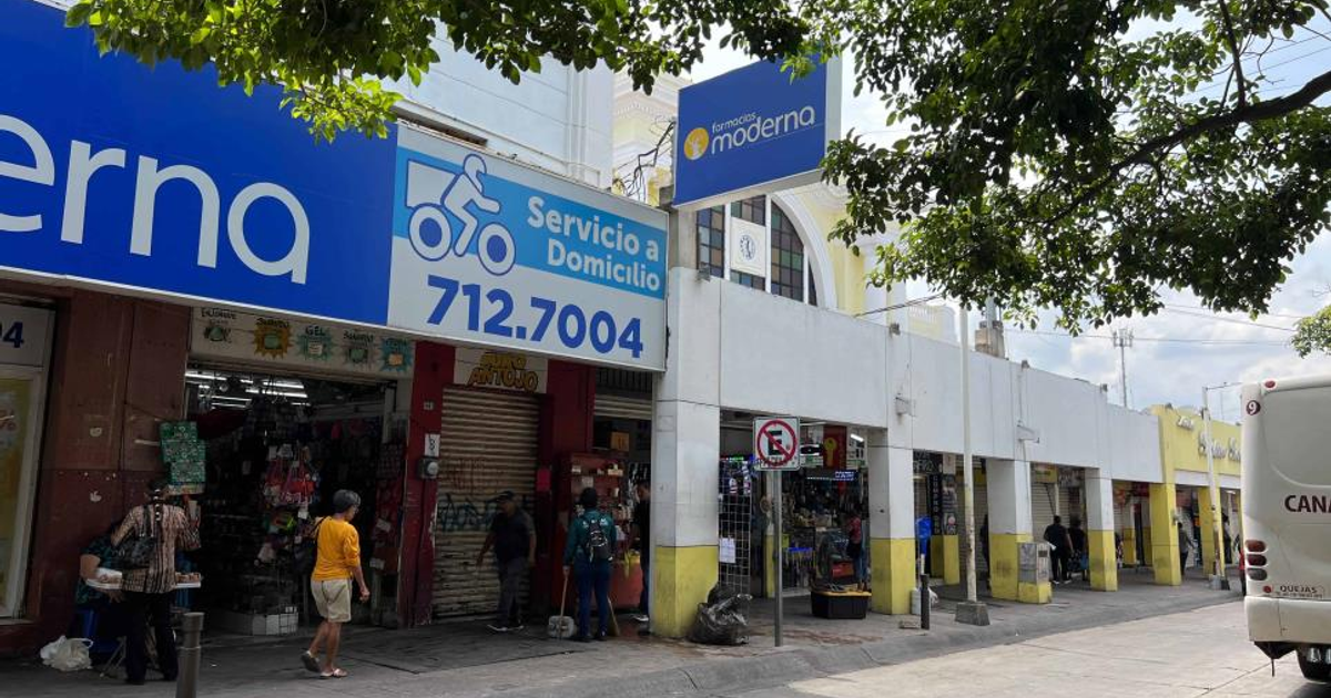 Calle comercial en Culiacán con letrero de 'Servicio a Domicilio', personas y autobús blanco.