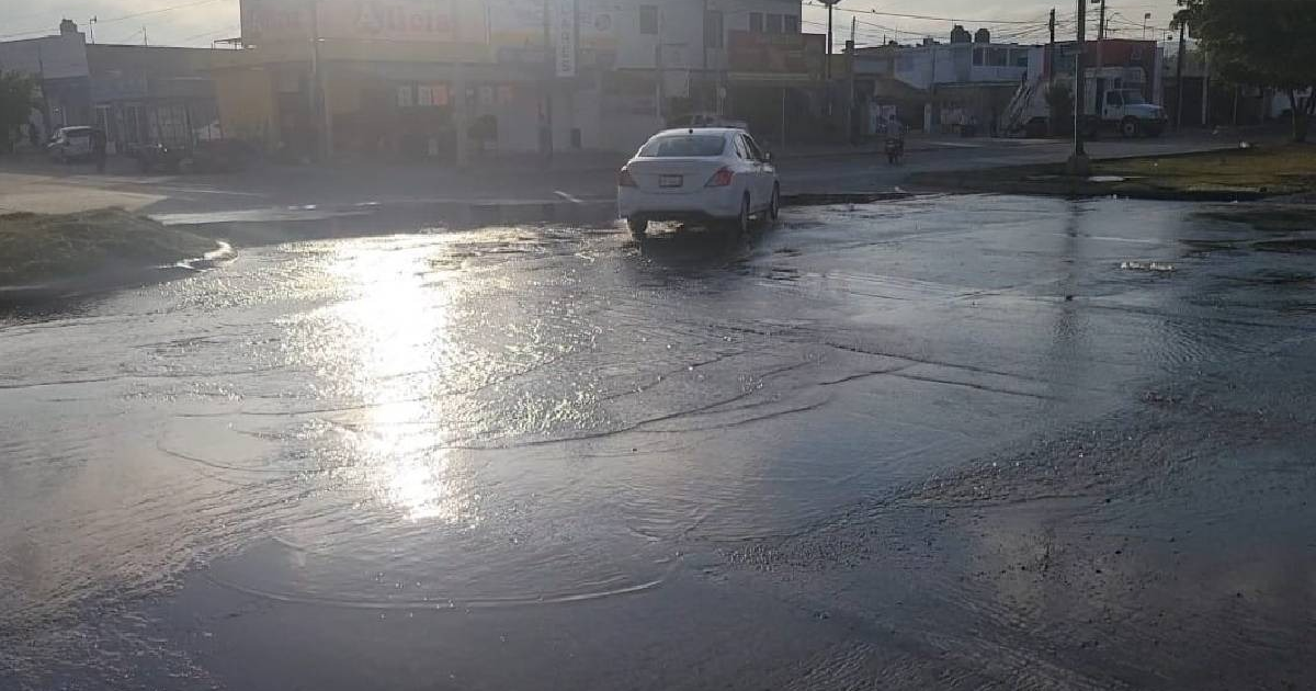 Calle mojada con vehículo blanco estacionado y edificios al fondo