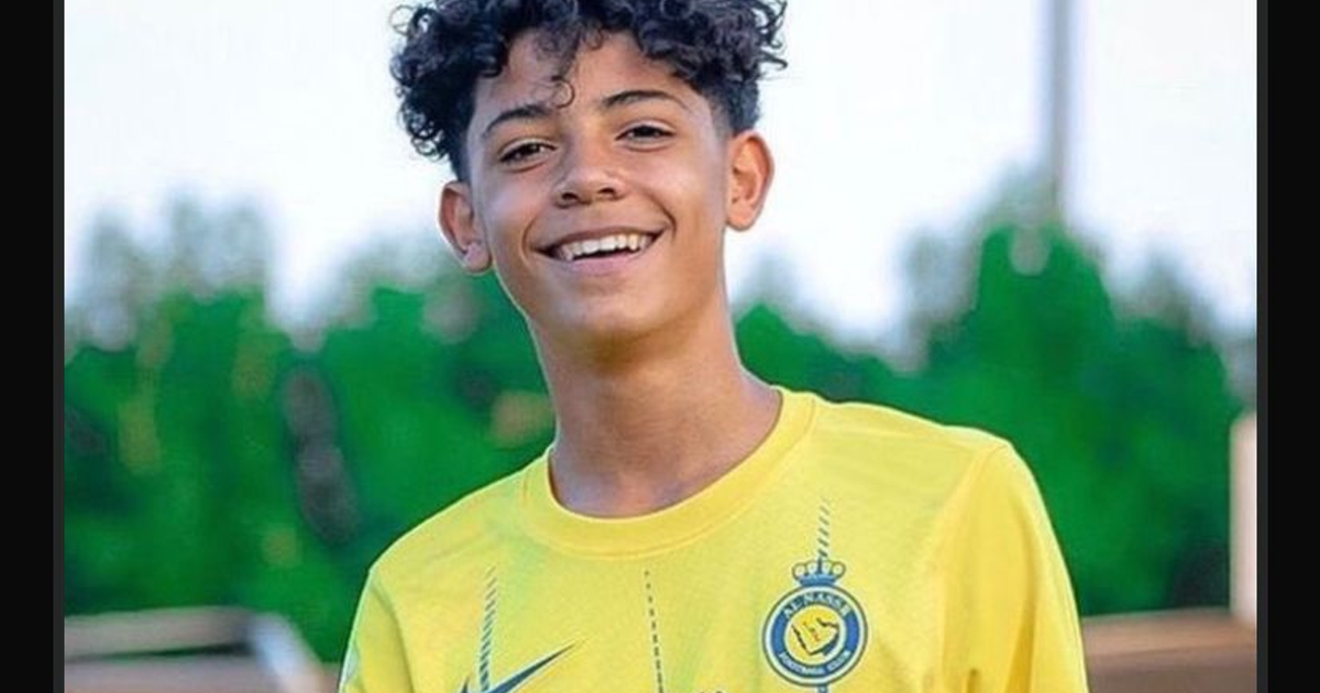 Cristiano Ronaldo Jr. sonriente con camiseta amarilla, fondo verde desenfocado