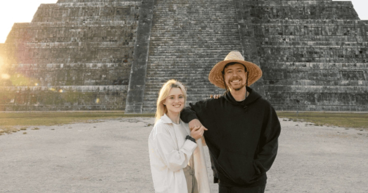 Dos personas sonrientes frente a una pirámide al atardecer en un sitio arqueológico.