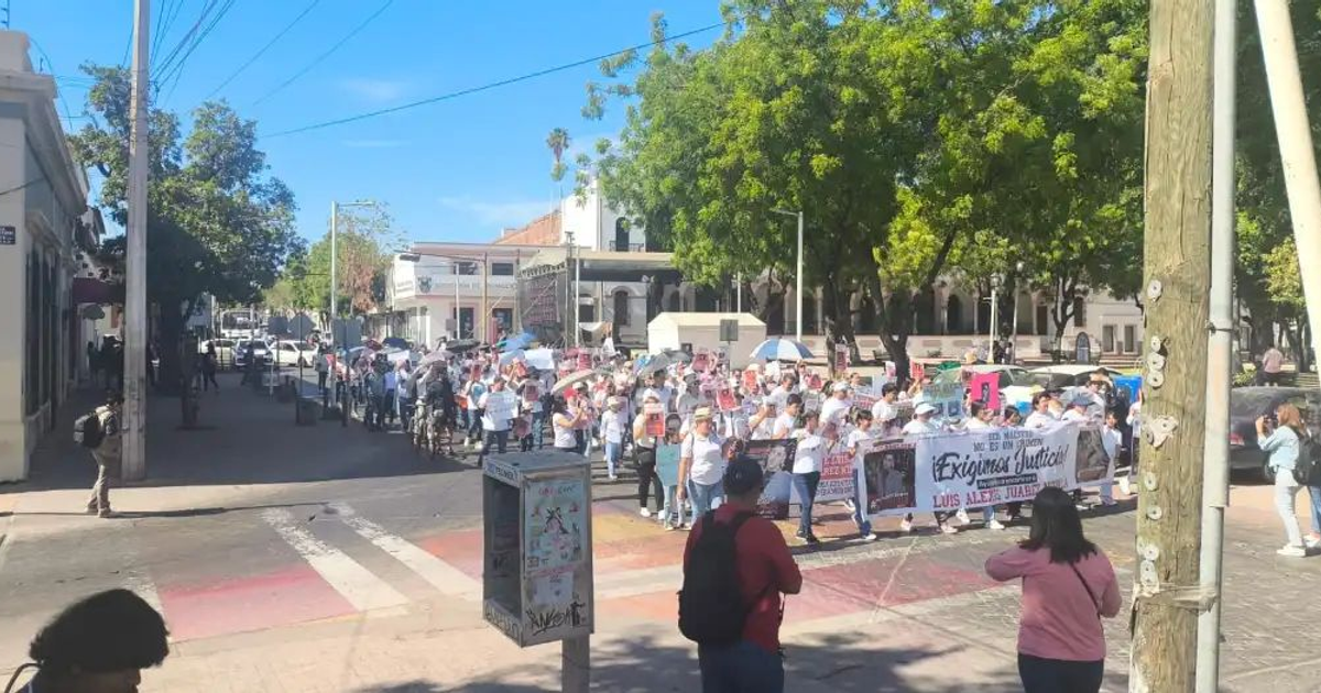 Manifestación en Culiacán por la desaparición del profesor Luis Alexis Juárez Niebla, con participantes sosteniendo carteles y una pancarta de 'Exigimos justicia'.