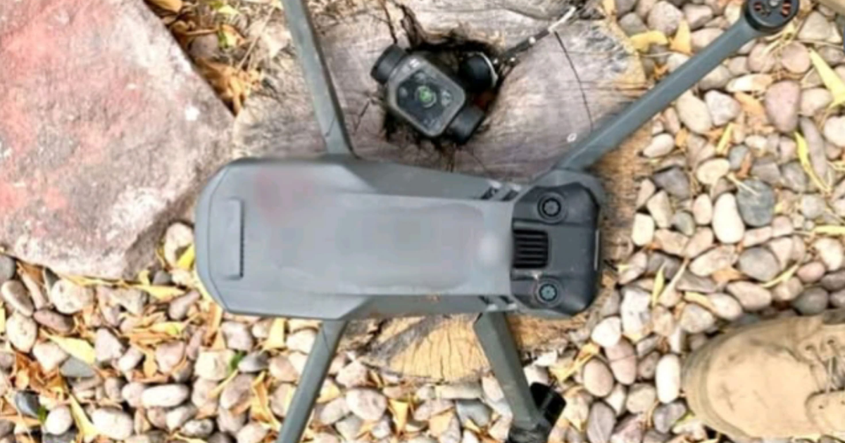 Dron en superficie de madera con cámara, piedras, hojas y bota visible