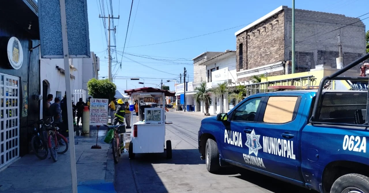 Calle en Escuinapa con vehículo de policía y carretilla de comida tras explosión en marisquería.