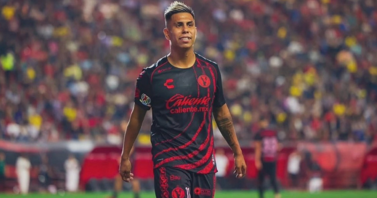Efraín Álvarez en el estadio con camiseta negra y detalles rojos, rodeado de espectadores.