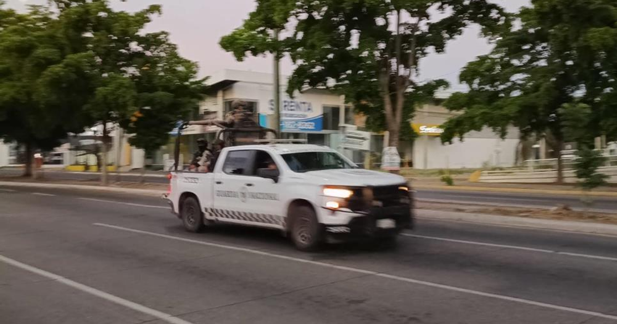 Camioneta blanca de la Guardia Nacional en movimiento por una calle con árboles y edificios al fondo.