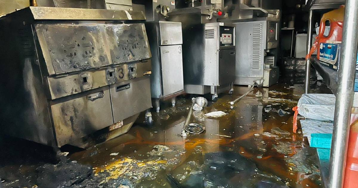 Cocina dañada por incendio en pizzería de Los Mochis, con equipos quemados y suelo desordenado.