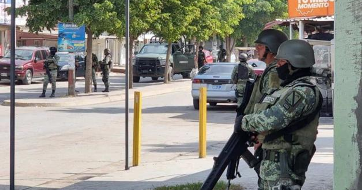 Fuerzas de seguridad armadas en vigilancia en una calle urbana con vehículos en movimiento.