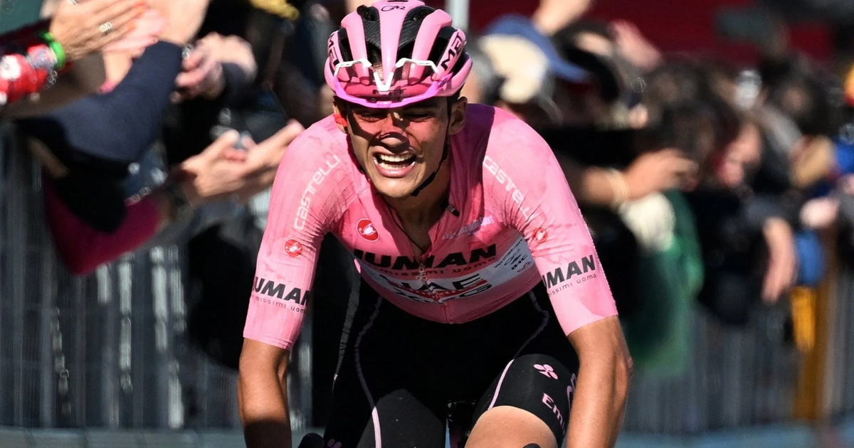 Ciclista con uniforme rosa compitiendo en una carrera, con espectadores al fondo.