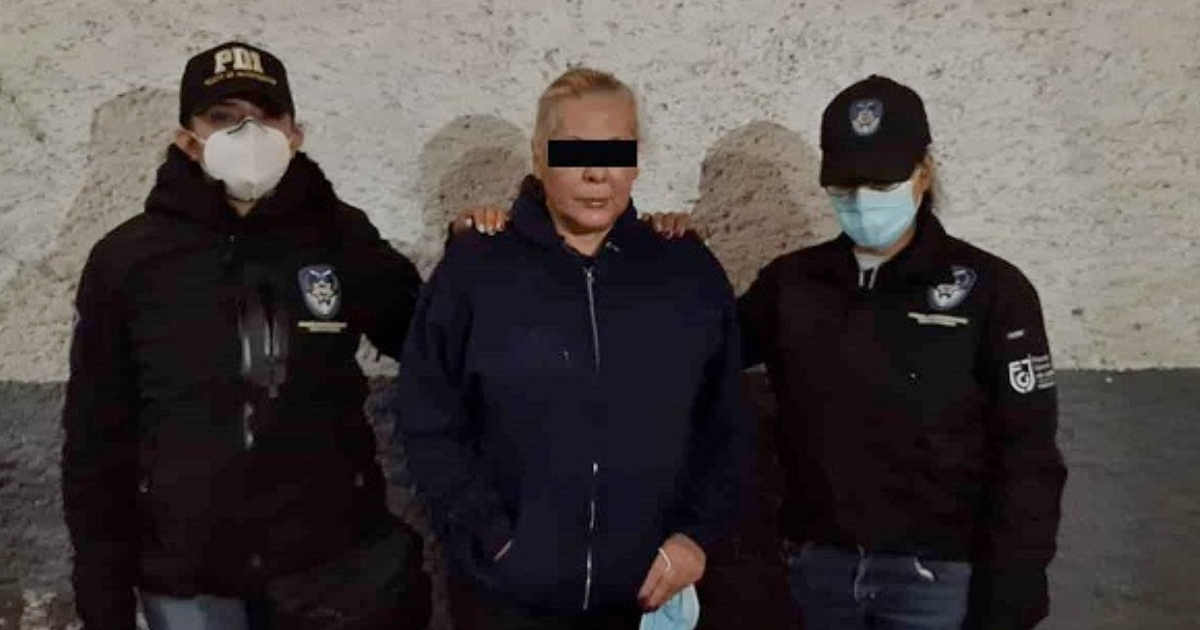 Dos policías posan con un detenido en un lugar oscuro, con una pared iluminada detrás.