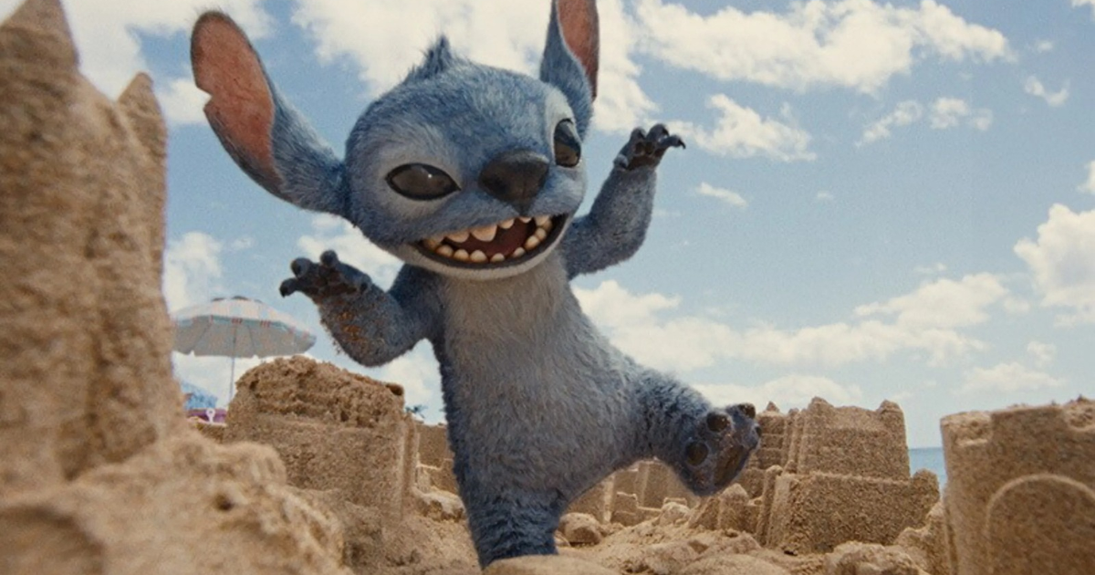 Stitch en la playa rodeado de castillos de arena y un cielo azul con nubes.