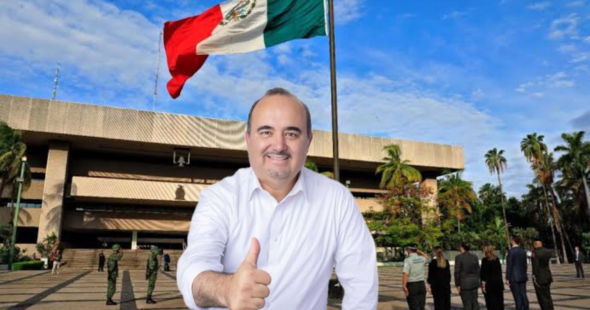 Guillermo 'Memo' Romero sonriendo con pulgar arriba frente a un edificio con bandera de México.