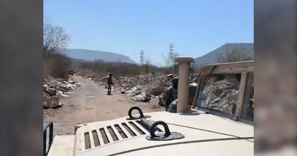 Camino de tierra en Culiacán con escombros, figura humana y vehículo militar, relacionado con un hallazgo trágico.