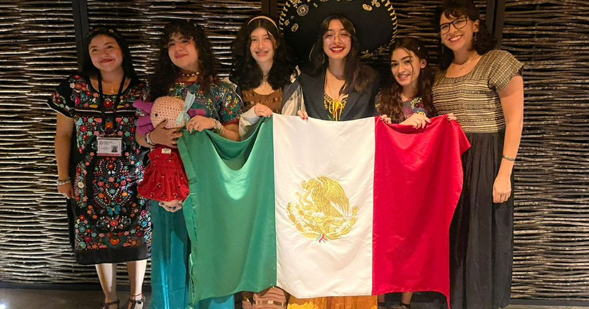 Grupo de personas con vestimenta tradicional mexicana sosteniendo una bandera de México en un evento festivo.