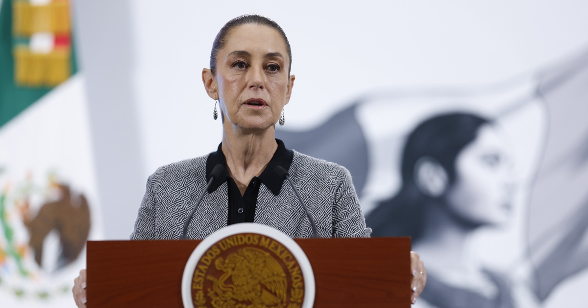 Claudia Sheinbaum en conferencia sobre paro de gaseros, con bandera de México y retrato en fondo.