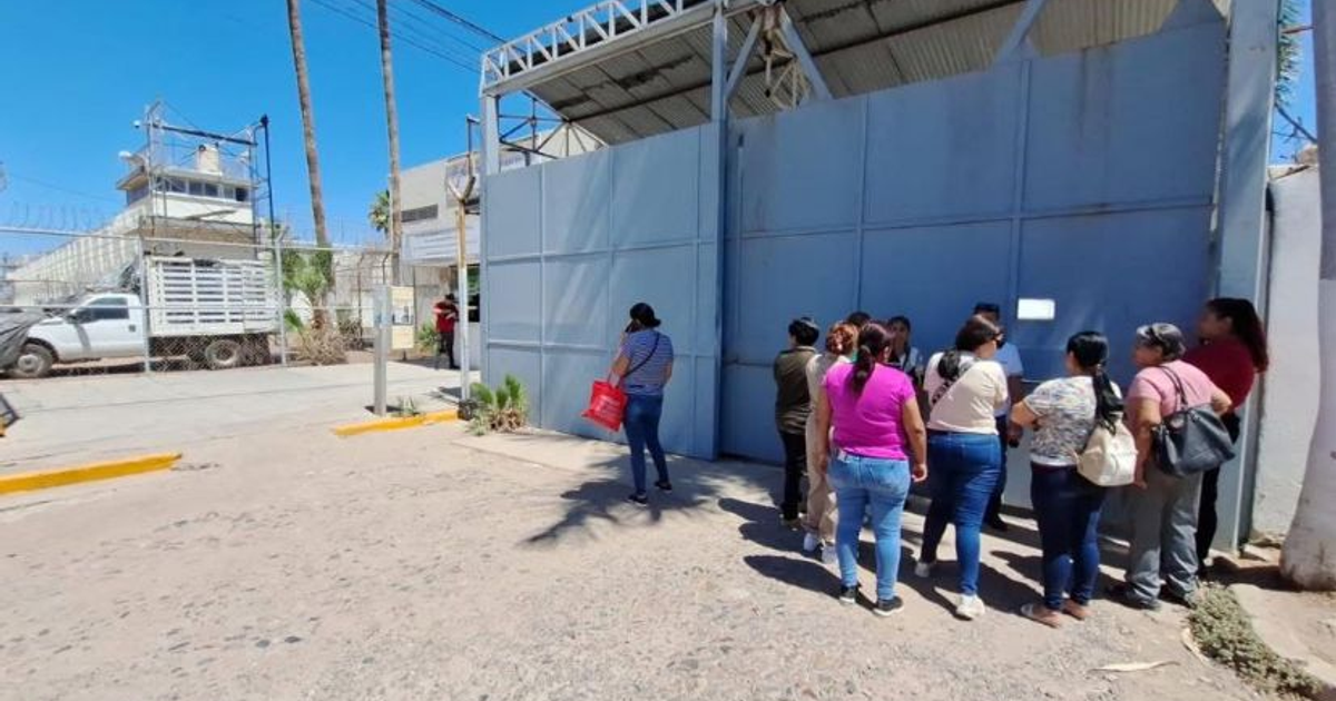 Grupo de personas en fila frente a una puerta azul en el penal de Aguaruto, esperando tras la suspensión de visitas.