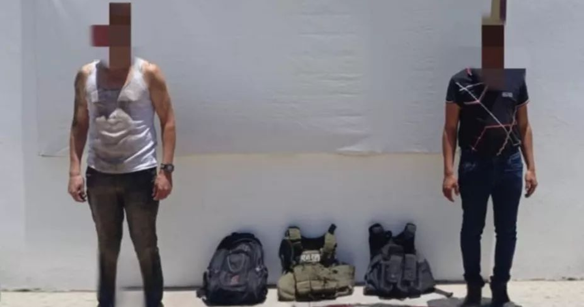 Dos personas con rostros pixelados de pie, mochilas y chalecos en el suelo, fondo blanco.