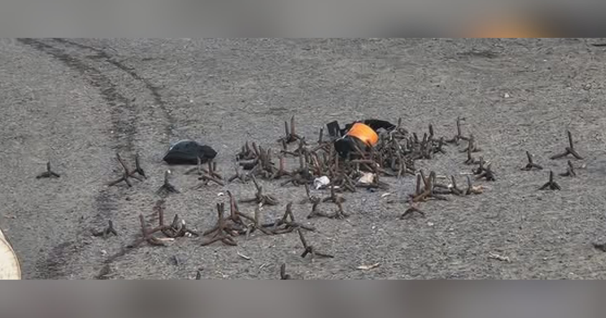 Área de suelo con estacas metálicas y objetos dispersos, vinculada a incidentes de ponchallantas en carretera.