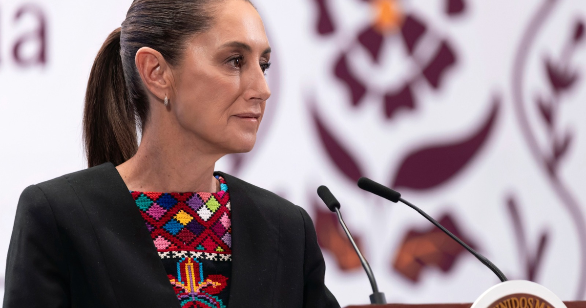 Mujer de perfil con coleta y blusa negra, hablando al micrófono, fondo florido.