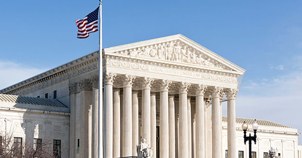 Edificio clásico con columnas y bandera de EE.UU. ondeando bajo un cielo despejado.