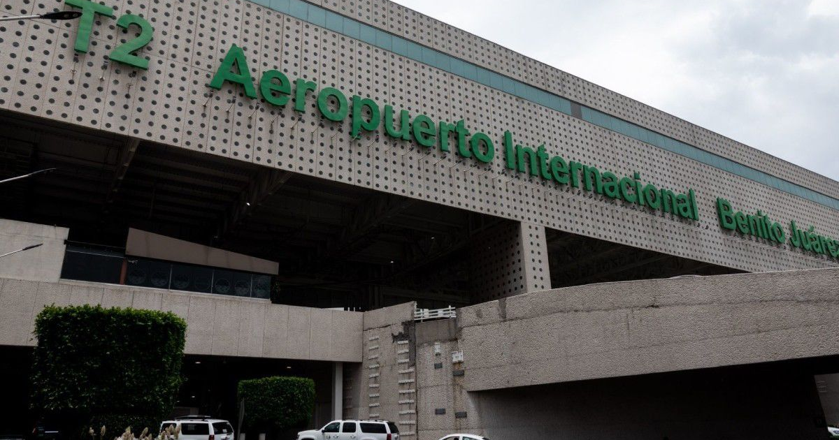 Fachada de la Terminal 2 del Aeropuerto Internacional Benito Juárez con diseño moderno y vegetación, bajo un cielo nublado.