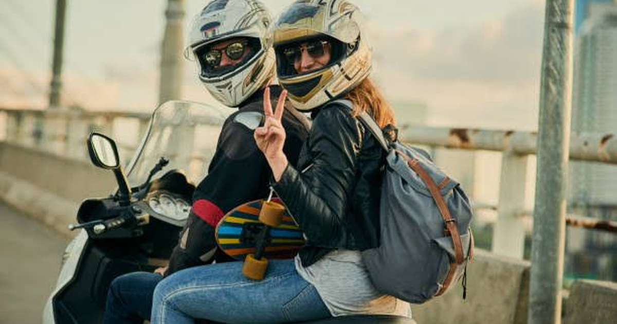 Dos personas en motocicleta con cascos y patineta en entorno urbano