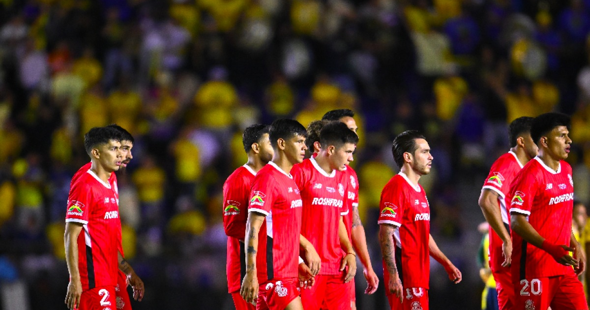 Jugadores de fútbol con uniformes rojos en el campo, fondo con público en colores amarillos.
