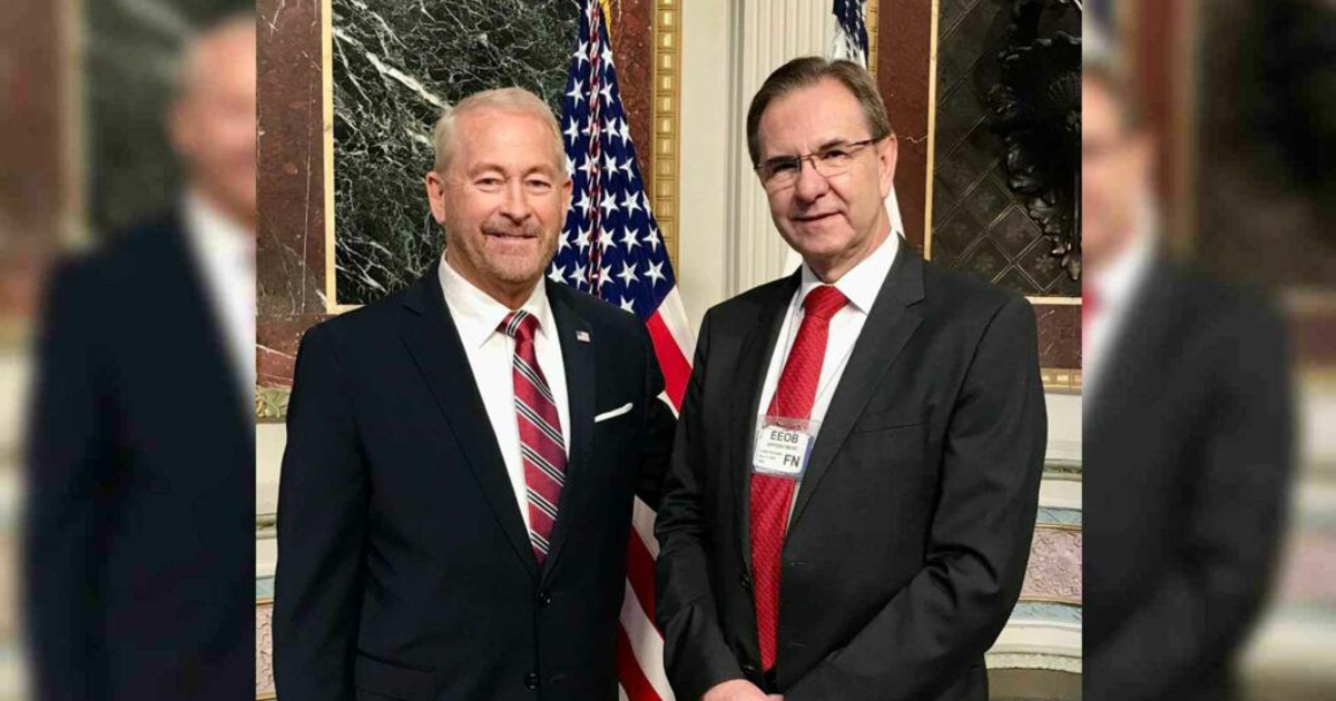 Dos diplomáticos sonrientes en trajes formales frente a una bandera de Estados Unidos, simbolizando la alianza México-Estados Unidos.