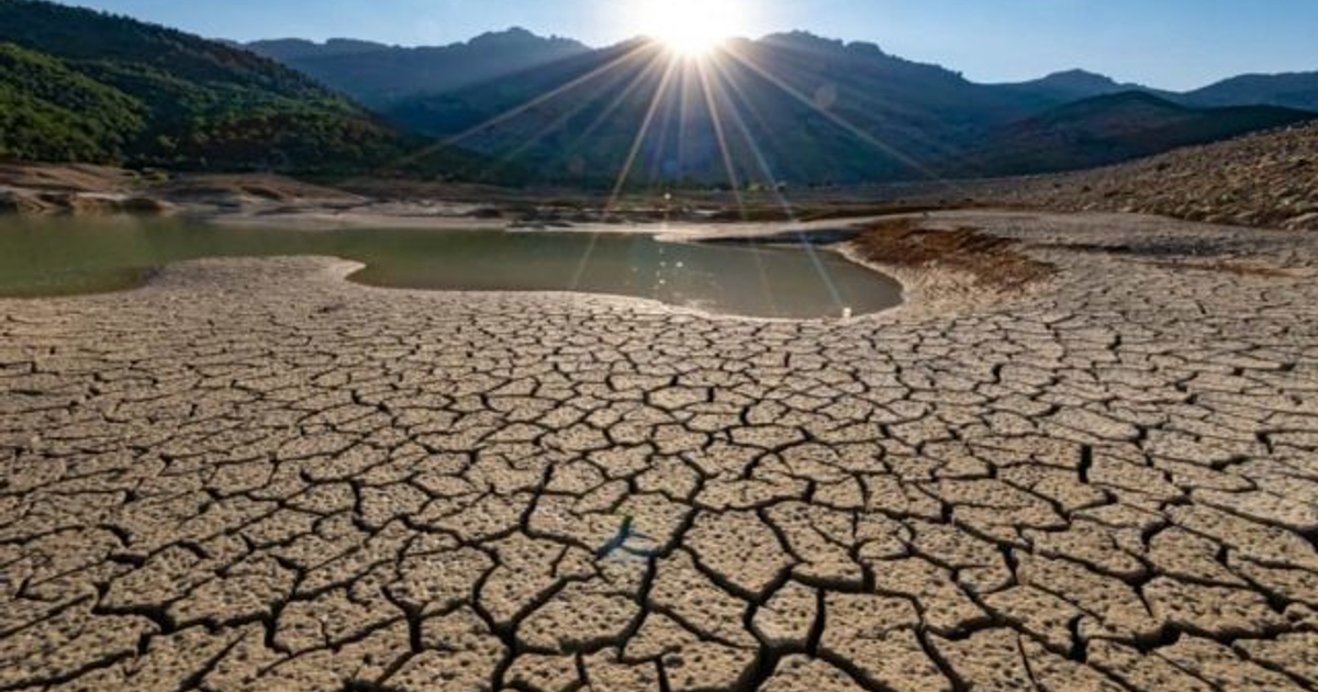 Terreno árido y agrietado en Sinaloa con montañas al fondo y un pequeño cuerpo de agua visible.