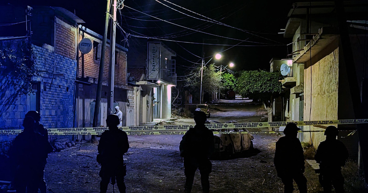 Escena nocturna en calle con edificios, vehículo, cinta de seguridad y personal uniformado.