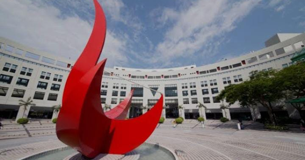 Escultura roja en forma de llamas en un espacio urbano de Hong Kong, junto a un edificio moderno.