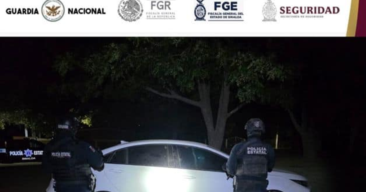 Dos policías junto a un automóvil blanco en un operativo nocturno en Agua Blanca, Sinaloa.