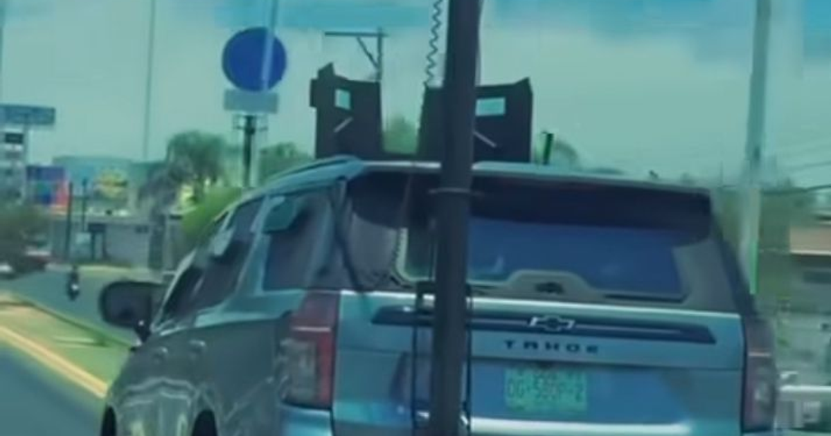 Chevrolet Tahoe blindado en una vía urbana con estructuras traseras oscuras y un letrero de tráfico al fondo.