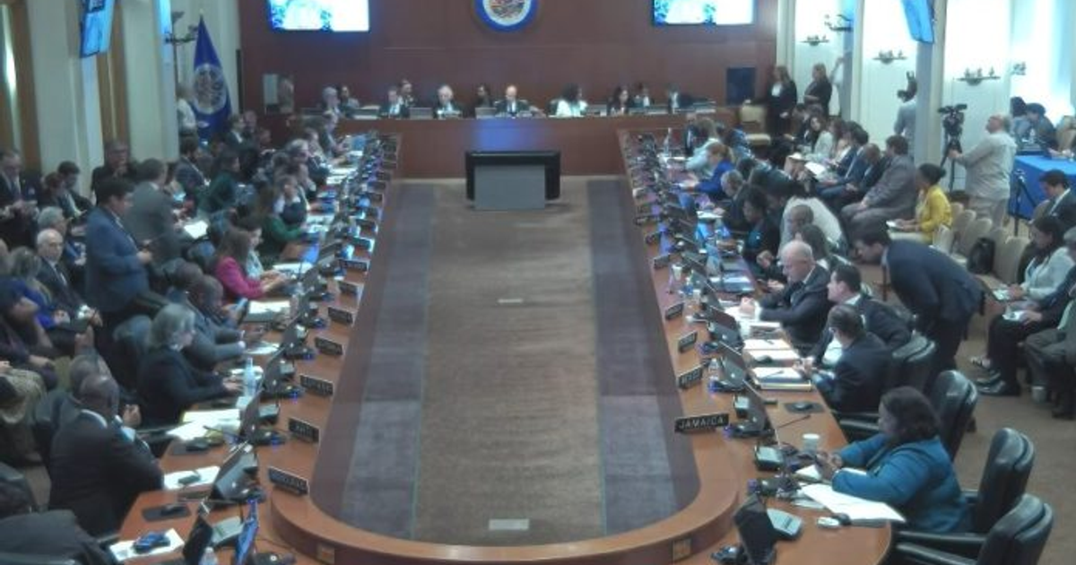 Conferencia de la Administración Trump en la Asamblea General de la OEA con participantes atentos y banderas en el fondo.