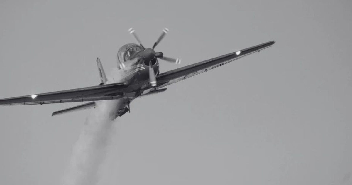 Avión en vuelo ascendente con estela de humo en blanco y negro