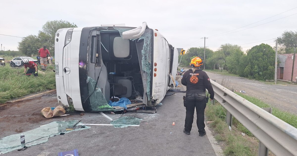 Accidente de autobús volcado en carretera con bombero y vehículos de emergencia presentes.