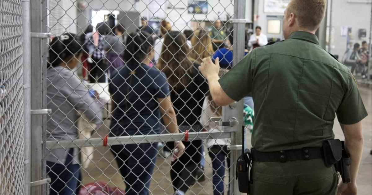 Agente de seguridad en centro de detención observando a mujeres detrás de una cerca de metal.