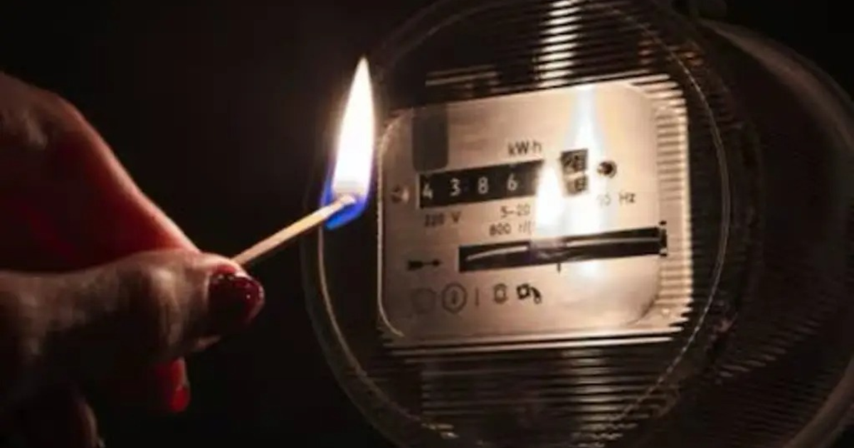 Mano con fósforo encendido iluminando un medidor de electricidad en la oscuridad