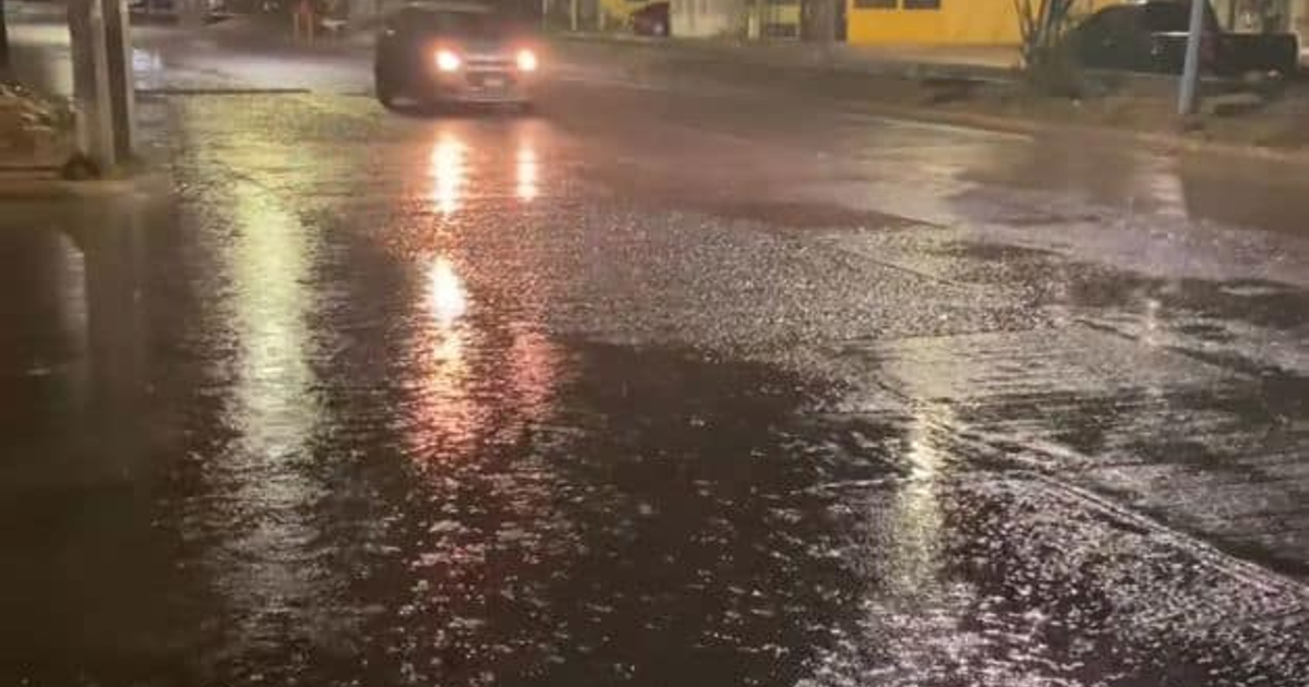 Calle de Mazatlán inundada por lluvias nocturnas, reflejando luces y un coche en movimiento.