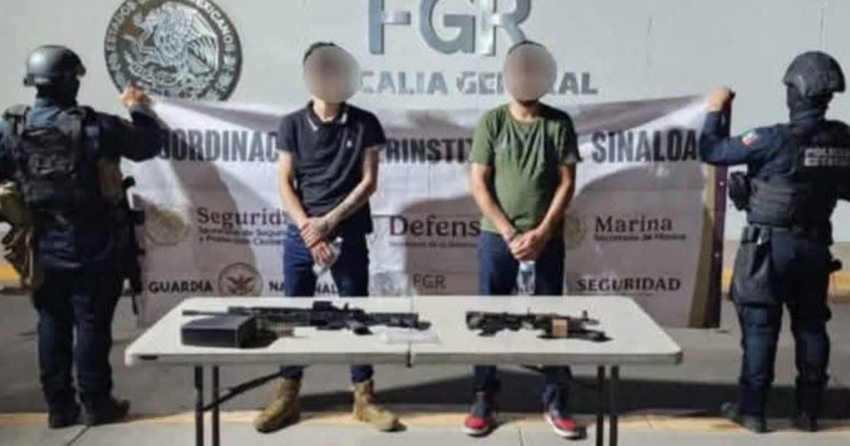 Dos personas detenidas frente a una mesa con armas, custodiadas por agentes de seguridad en Navolato.