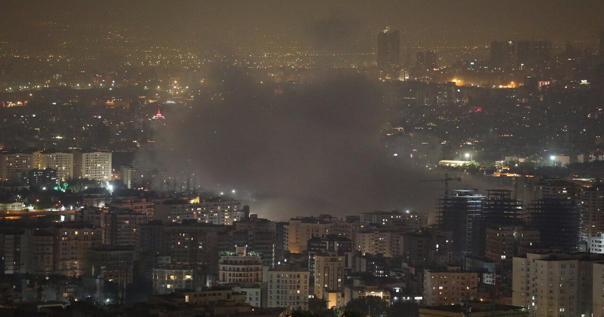 Vista nocturna de una ciudad iluminada con humo en el centro, relacionada con el conflicto Israel-Irán.