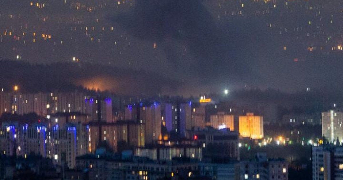 Vista nocturna de Teherán con edificios iluminados y humo en el horizonte