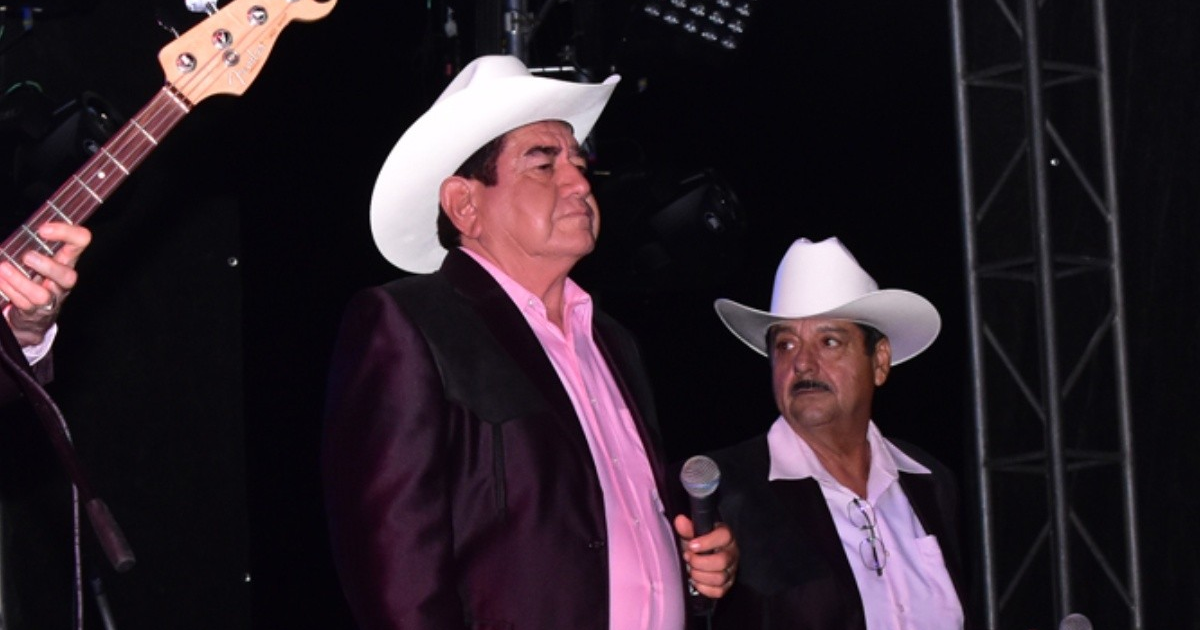 Dos músicos en el escenario con sombreros blancos y trajes oscuros durante un evento benéfico para David Higuera.