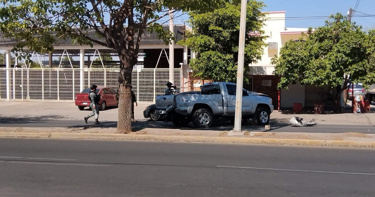 Camioneta azul y coche rojo estacionados en una calle urbana con una persona en uniforme caminando.