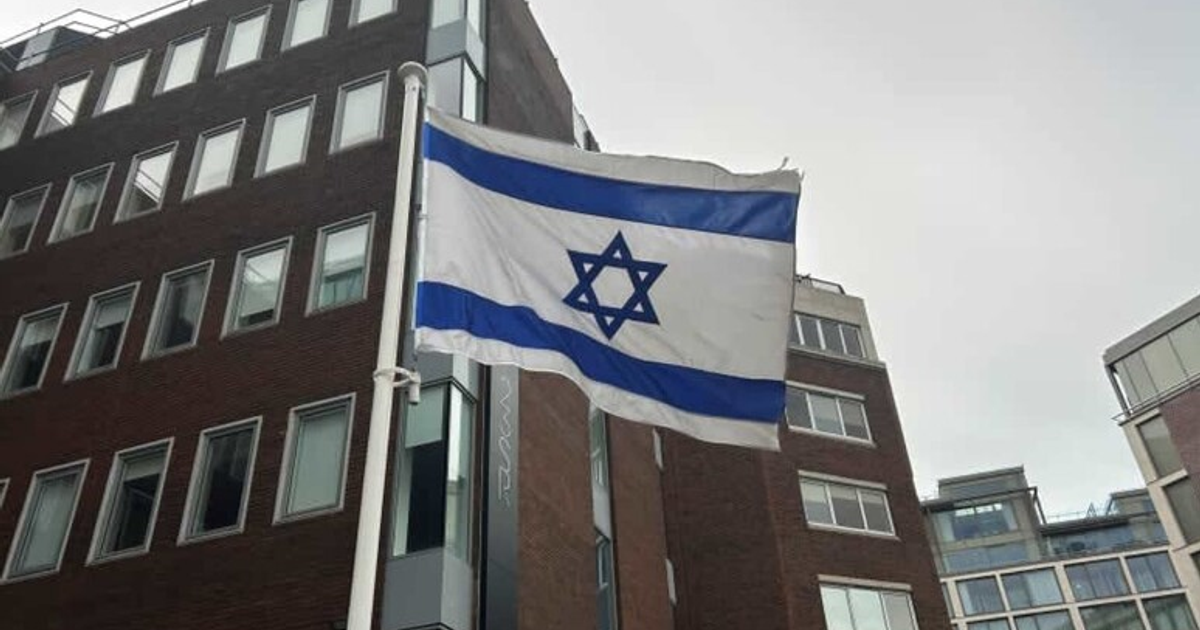 Bandera de Israel ondeando frente a un edificio con ventanas